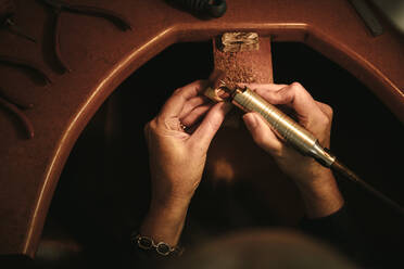 Nahaufnahme der Hände einer Juwelierin, die einen Ring an ihrer Werkbank poliert. Goldschmiedin, die die Oberfläche eines Rings mit einer Schleifmaschine in der Werkstatt nahtlos macht. POV-Aufnahme. - JLPSF18586