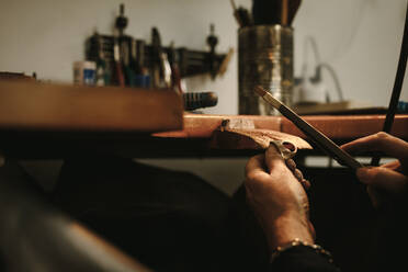 Close up of female goldsmith making gold ring at workshop. Female jeweler using tools to shape a golden ring at her workbench. - JLPSF18587