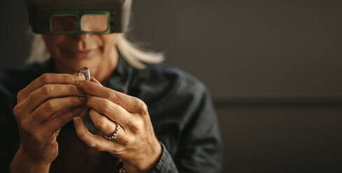 Female goldsmith inspecting jewelry using magnifying glass in workshop. Woman jeweler inspecting diamond ring with magnifying glass. - JLPSF18589