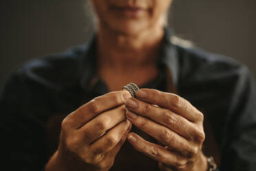 Nahaufnahme der Hände einer Juwelierin, die einen Ring in einer Werkstatt prüft. Fokus auf die Hände einer Juwelierin, die einen Silberring prüft. - JLPSF18591