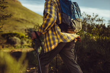 Mann wandert mit Trekkingstöcken einen Berg hinauf. Ausschnitt aus der Seitenansicht eines Mannes, der mit Rucksack einen Berg hinaufgeht. - JLPSF18635