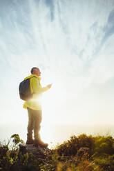 Hiker standing on a hill enjoying the view with sun in the background. Man standing relaxed after finishing his trek on a hill. - JLPSF18645