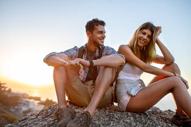 Man and woman hikers relaxing on hill top. Hiker couple taking a break sitting on rock and smiling. - JLPSF18657