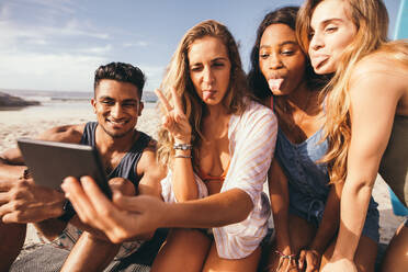 Nahaufnahme einer Gruppe von Freunden am Strand, die ein Selfie mit dem Handy machen. Fröhliche Freunde im Urlaub machen Gesichter und strecken die Zunge heraus, während sie ein Selfie machen. - JLPSF18659