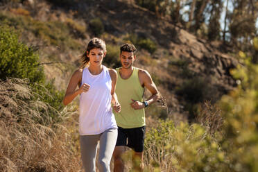 Healthy young couple running on mountain trail in morning. Young man and woman jogging on country path. - JLPSF18660