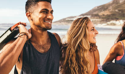 Smiling couple walking together on beach on a sunny day. Close up of a smiling man with his girlfriend at the beach with sea in the background. - JLPSF18675