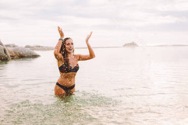 Lächelnde Frau im Bikini, die im Wasser plantscht und sich im Meer vergnügt. Fröhliche Frau im Urlaub, die Spaß beim Baden im Meer hat. - JLPSF18685