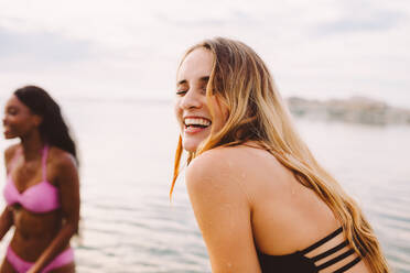 Close up of a smiling woman playing in the sea with friends. Friends on a holiday enjoying at the beach on a cloudy day. - JLPSF18687