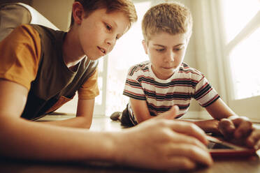 Zwei Jungen spielen mit großem Interesse ein Spiel auf einem Tablet-PC. Kinder liegen zu Hause auf dem Boden und benutzen einen Tablet-PC. - JLPSF18700