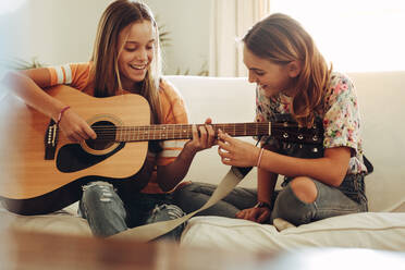 Zwei lächelnde Mädchen im Teenageralter lernen zu Hause Gitarre spielen. Mädchen spielen zu Hause Musik auf der Gitarre. - JLPSF18705