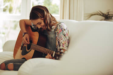 Lächelndes junges Mädchen, das zu Hause auf der Gitarre musiziert. Teenager-Mädchen lernt Gitarre spielen. - JLPSF18708