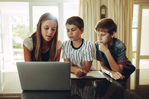 Jungen und ein Mädchen, die zu Hause auf einen Laptop schauen und lernen. Junges Mädchen im Teenageralter, das Jungen an einem Laptop Schulunterricht erteilt. - JLPSF18709