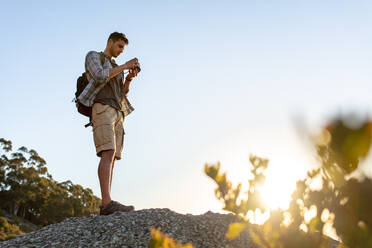 Mann steht mit Digitalkamera auf dem Gipfel eines Berges und prüft die Bilder. Männlicher Wanderer, der eine Landschaft vom Berggipfel aus fotografiert. - JLPSF18756