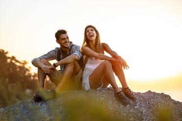 Junges Paar, das auf einer Wanderung eine Pause einlegt. Glücklicher junger Mann und Frau, die auf einem Berggipfel sitzen und lachen. - JLPSF18758