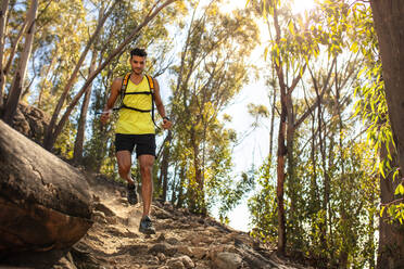 Fit junger Mann in Sportkleidung trägt Trinkrucksack läuft im Freien über felsigen Weg auf dem Hügel. Berg Trail Läufer üben auf Feldweg. - JLPSF18768