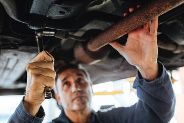 Automechaniker festziehen Auspuffanlage Rohr unter dem Auto. Autoreparatur Männer ein Auto in Service-Station zu reparieren. Fokus in Mechaniker Hand mit Schraubenschlüssel Schraubenschlüssel. - JLPSF18780