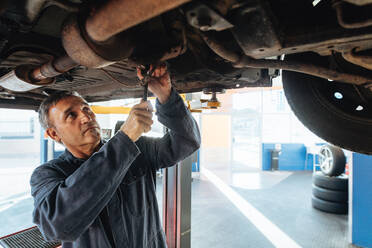 Automechaniker bei der Arbeit unter einem Auto in einer Werkstatt. Automechaniker bei der Reparatur eines Fahrzeugs in einer Tankstelle. - JLPSF18784