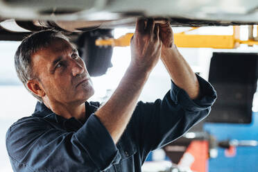Automechaniker, der ein angehobenes Auto in einer Garage repariert. Autowerker, die ein Auto in einer Tankstelle reparieren. - JLPSF18800