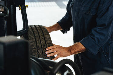 Cropped shot of a mechanic checking the condition of a automobile wheel. Man examining the wear and tear of car tire in garage. - JLPSF18803