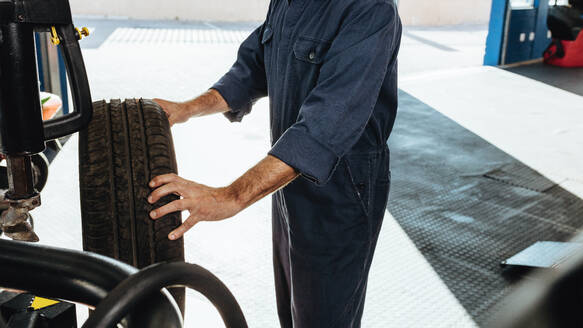 Ausschnitt eines Mechanikers bei der Überprüfung von Autoreifen an einer Maschine in einer Servicestation. Ein Mann prüft den Reifengriff in einer Werkstatt. - JLPSF18804