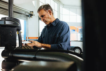 Mechanic checking the car wheel surface on machine. Technician working in automobile tyre mounted on machine in garage. - JLPSF18805