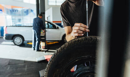 Mechanic checking car tire tread depth with caliber. Technician examining the car tire grip with a measuring instrument in service station. - JLPSF18806