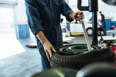 Mechaniker wechselt Autoreifen auf einer Reifenwechselmaschine in der Werkstatt. Ausschnitt von Mechanikerhänden, die den Reifen von der Scheibe der Maschine entfernen. - JLPSF18812