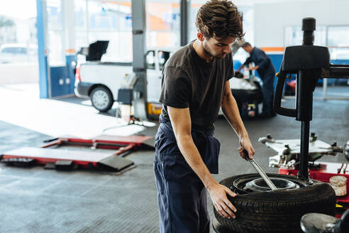 Ein Mechaniker wechselt einen Reifen in einer Werkstatt. Ein Mechaniker wechselt einen Autoreifen in einer Tankstelle. - JLPSF18815