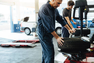 Mechanics working in car repair workshop. Auto repair workers working on tire replacing machine in auto repair shop. - JLPSF18816