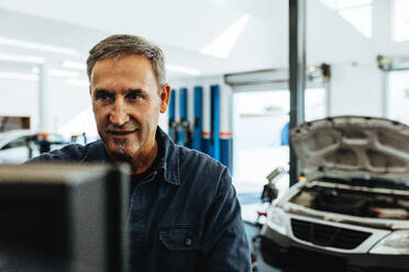 Mature male mechanic checking a car with computer. Mechanic doing car diagnostic on computer. - JLPSF18819