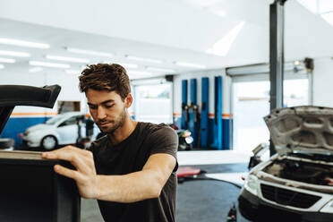 Young mechanic doing car check up on computer. Mechanic using computerized equipment to diagnose a car in service station. - JLPSF18820