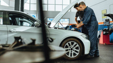 Automobile technicians using electronic diagnostic equipment to tune a car. Mechanics using a device to check the engine. - JLPSF18824