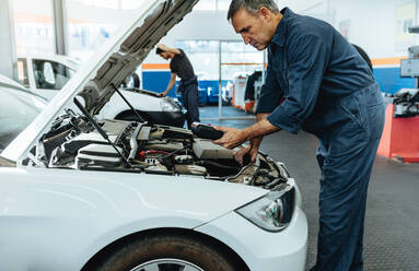 Automechaniker mit Diagnosegerät zum Ablesen der Fehlercodes. Mechaniker bei der Überprüfung des Autos in der Werkstatt. - JLPSF18825