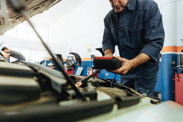 Techniker, der mit Hilfe eines elektronischen Diagnosegeräts den Motor eines Fahrzeugs überprüft. Mechaniker, die ein Gerät zur Überprüfung des Motors verwenden. - JLPSF18828