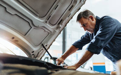 Male mechanic repairing the car in auto service center. Mechanic in uniform fixing a vehicle. - JLPSF18832