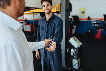 Mechanic receiving car keys from customer in automobile service center. Customer giving his car keys to mechanic at the repair garage. - JLPSF18838