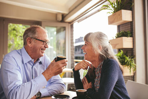 Fröhliches älteres Paar, das sich bei einer Tasse Kaffee im Café unterhält. Ein Mann und eine Frau im Ruhestand sitzen in einem Café und unterhalten sich bei einem Kaffee. - JLPSF18848
