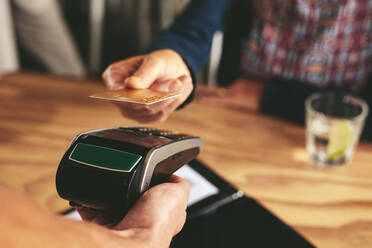 Ein Kunde, der mit seiner Kreditkarte kontaktlos bezahlt. Ein Kassierer hält ein Kreditkartenlesegerät, das die Zahlung über NFC-Technologie akzeptiert. - JLPSF18855