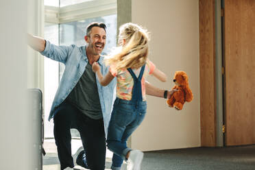 Ein Mädchen läuft mit einem Teddybär in der Hand auf ihren Vater zu, der gerade von einer Geschäftsreise zurückkommt. - JLPSF18867