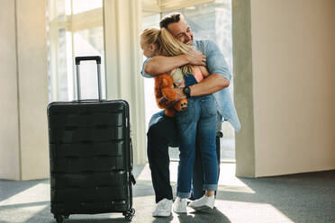 Mädchen begrüßt ihren Vater an der Tür, wenn er von einer Reise zurückkommt. Tochter umarmt ihren Vater, der gerade mit einem Reisekoffer von einer Geschäftsreise zurückkommt. - JLPSF18868