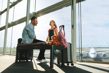 Familie am Flughafen wartet auf den Abflug. Vater und Tochter sitzen mit ihrem Gepäck in der Flughafenlounge und warten auf ihren Flug. - JLPSF18876