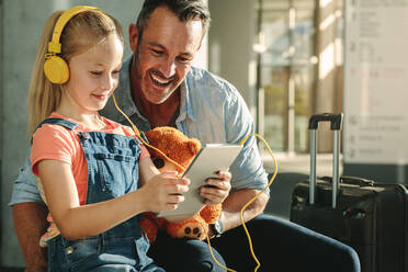 Glücklicher Vater und Tochter, die einen Tablet-Computer in der Flughafen-Lounge benutzen, während sie auf ihren Flug warten. Mädchen, das mit ihrem Vater in der Warte-Lounge des Flughafens einen Tablet-PC benutzt. - JLPSF18880