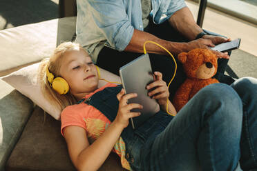 Mädchen mit Tablet-PC mit ihrem Vater sitzt auf der Seite mit einem Mobiltelefon am Flughafen Wartehalle. Familie entspannt am Flughafen Wartehalle. - JLPSF18881