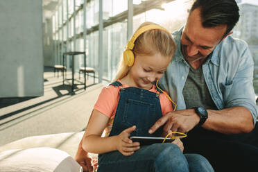 Vater und Tochter nutzen ein digitales Tablet in der Wartelounge eines Flughafens. Zwei Familienmitglieder in der Abflughalle eines Flughafens nutzen einen Tablet-Computer. - JLPSF18882