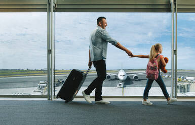 Mädchen hält die Hand ihres Vaters und geht zum Flughafen, um ihren Flug zu besteigen. Vater und Tochter fahren in den Urlaub. - JLPSF18883