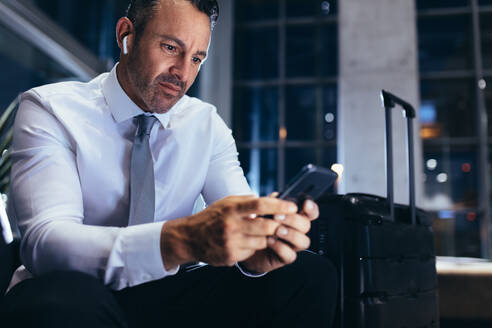 Geschäftsmann sitzt in der Flughafen-Lounge und schreibt eine SMS in sein Mobiltelefon. Geschäftsmann auf einer Geschäftsreise benutzt sein Mobiltelefon, während er auf seinen Flug wartet. - JLPSF18892