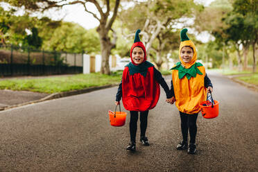 Two little girls in halloween costume trick or treating on the road. Two identical twin sisters in halloween costume walking outdoors with halloween bucket. - JLPSF18911