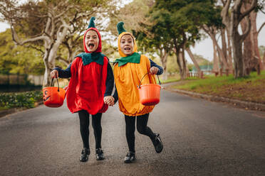 Niedliche kleine Mädchen in Halloween-Kostüm Trick oder Behandlung im Freien. Eineiige Zwillingsschwestern in Halloween-Kostüm mit Halloween-Eimer zu Fuß im Freien, - JLPSF18912