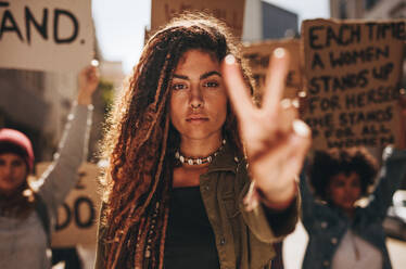 Frau zeigt ein Friedenszeichen während eines Protests. Frau mit einer Gruppe von Frauen, die im Freien auf einer Straße protestieren. - JLPSF18916