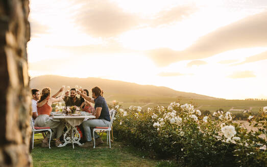 Group of friends toasting champagne glasses at dinner party outdoors. Young people having drinks during dinner at garden. - JLPSF18945